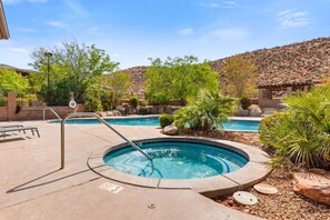A swimming pool area with a hot tub, surrounded by desert vegetation and a hilly backdrop.