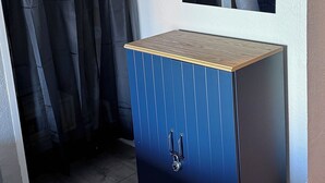A small, dark blue cabinet with a wooden top and a lock, positioned next to a window with a view of a room. - Beautiful condo with Ocean Views in vibrant Myrtle Beach (Myrtle Beach)