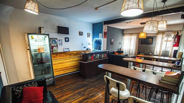A modern bar area with a counter, seating, and a refrigerator stocked with beverages.
