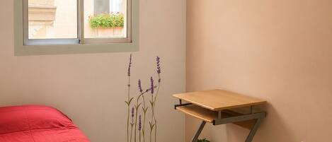 A bedroom with a bed, a window, a desk, and a wall decoration.