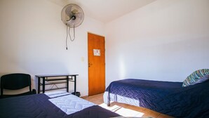 A room with two beds, a desk, a chair, and a standing fan.
