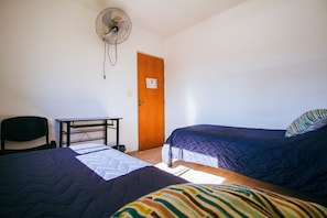 A room with two beds, a desk, a chair, and a standing fan. - Go Hostel (Córdoba)