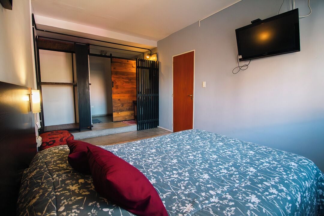 Un dormitorio con cama, televisión montada en la pared y puerta corredera que da a un espacio exterior.