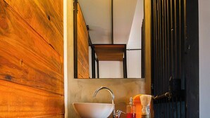 A bathroom with a wooden wall, a sink with a mirror, and a red rug.