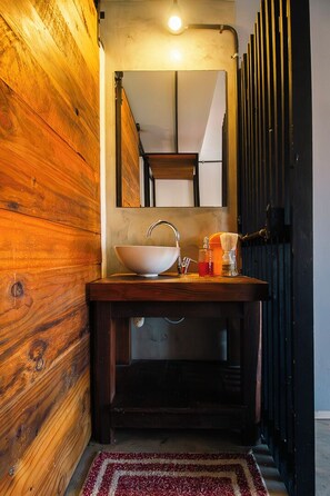 A bathroom with a wooden wall, a sink with a mirror, and a red rug. - Go Hostel (Córdoba)