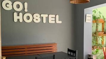 Ein Hostel-Interieur mit einer Holzbank, einem Tisch und Stühlen, und einem Schild mit der Aufschrift 'GO HOSTEL'.