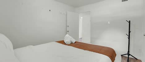 Une chambre d’hôtel avec un lit, un radiateur mobile et une porte donnant sur une autre pièce.