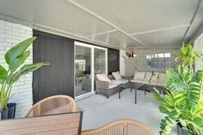 Ein überdachter Außenbereich mit Korbmöbeln und einer Glastür, die auf eine Terrasse führt.