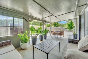 Ein überdachter Patio-Bereich mit Tisch und Stühlen, Topfpflanzen und Blick auf die Umgebung.