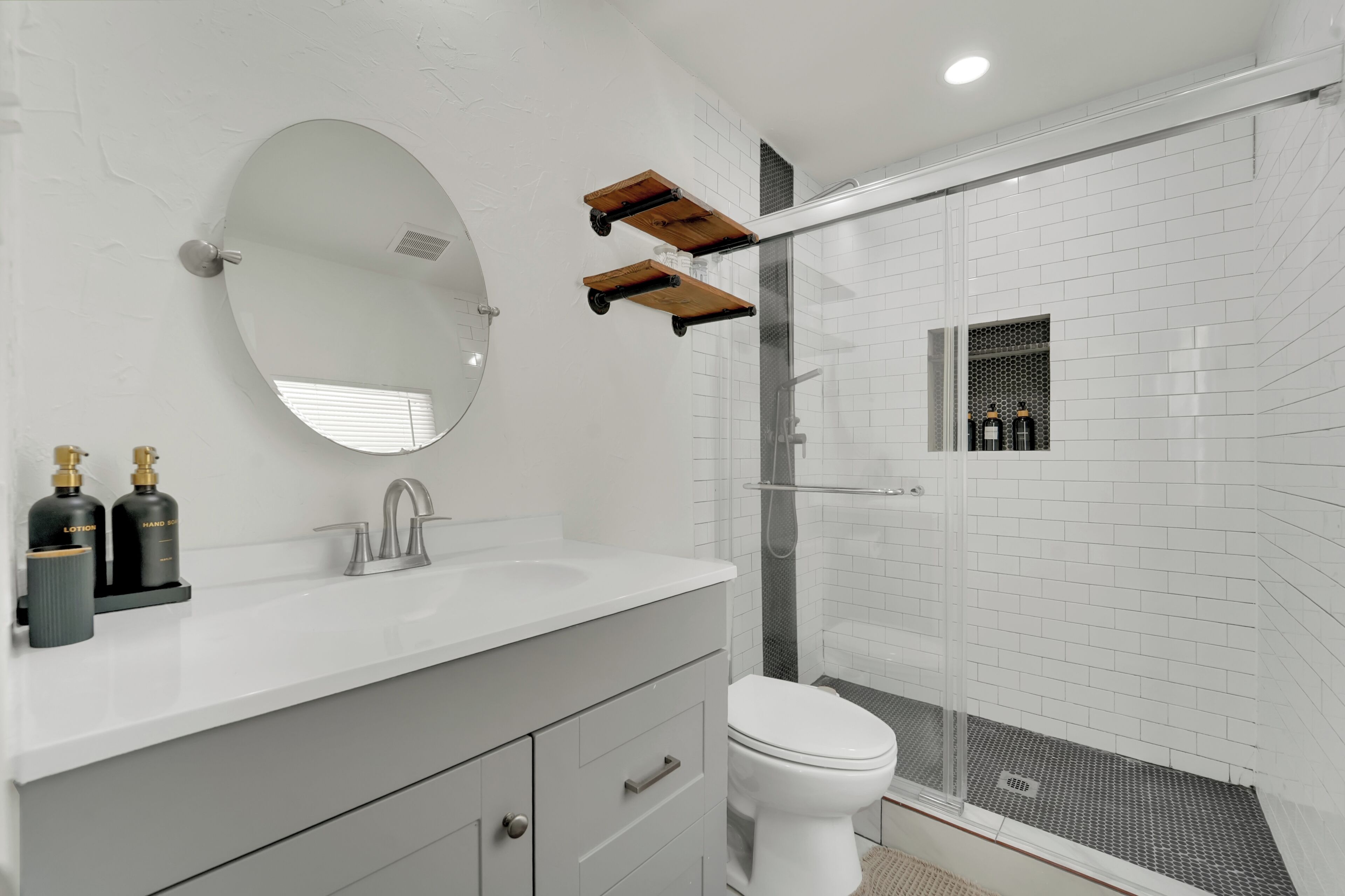 A modern bathroom with a white sink, a round mirror, a toilet, and a glass-enclosed shower area.