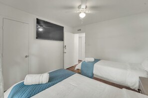 A hotel room with two beds, a ceiling fan, a television, and a door. - Spacious Entire Home •4BR  •7 Beds •Sleeps 12+ • Near Dallas, Plano, Richardson (Garland)
