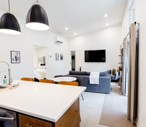 A modern hotel room with a dining area, a sofa, a flat-screen TV, and a large window.