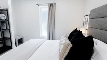 Une chambre d’hôtel avec un lit, une fenêtre avec des rideaux, une table de chevet avec une lampe et une tête de lit.
