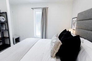 A hotel room with a bed, a window with curtains, a bedside table with a lamp, and a headboard.