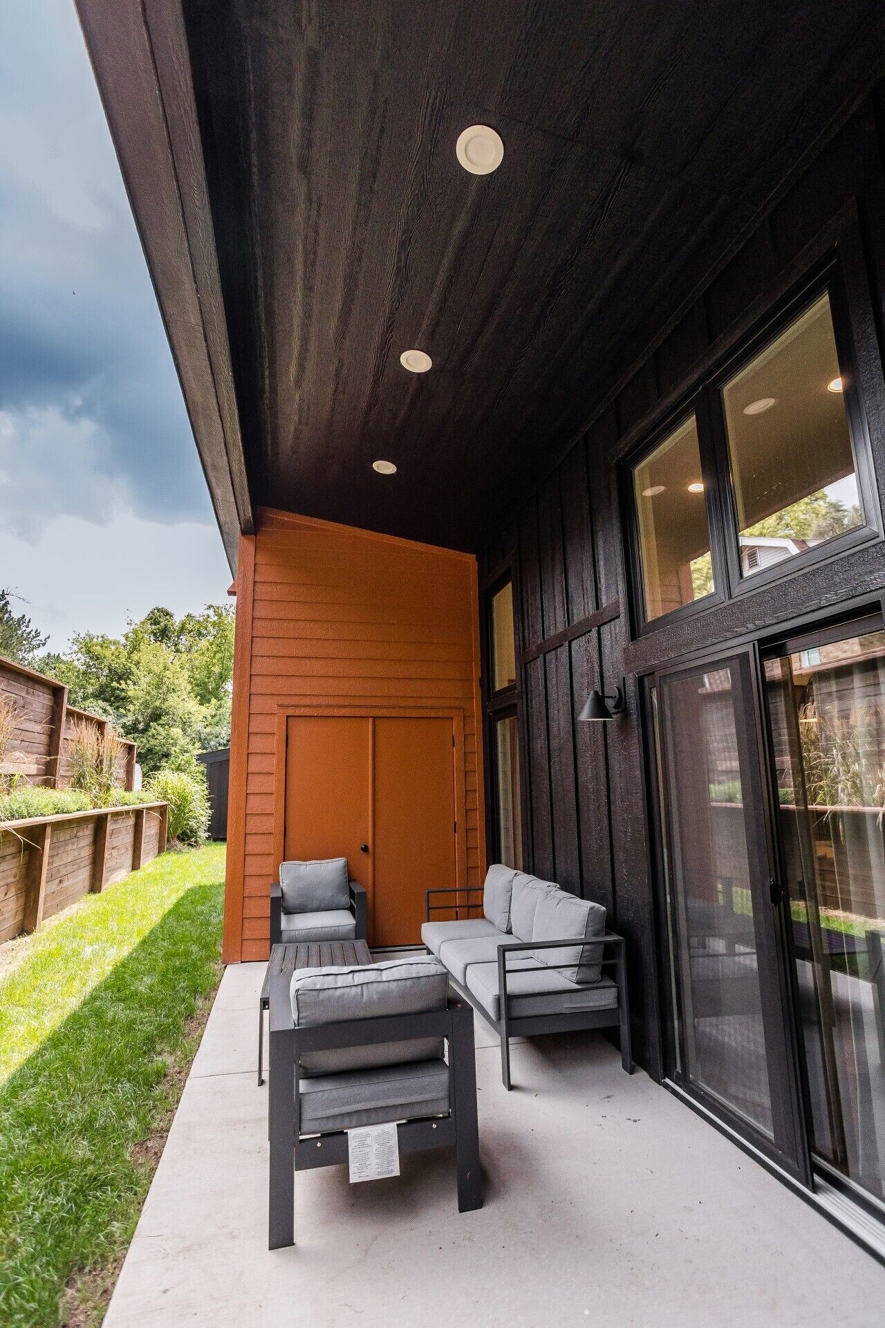 Un espacio al aire libre con sofá y sillones, una puerta de madera y un ventanal grande.