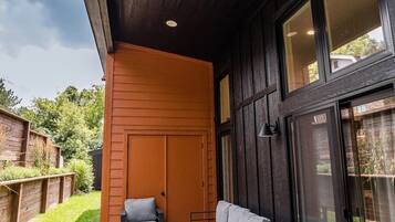 Un espacio al aire libre con sofá y sillones, una puerta de madera y un ventanal grande.