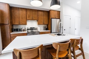 A modern kitchen with wooden cabinets, stainless steel appliances, and a central island with chairs.