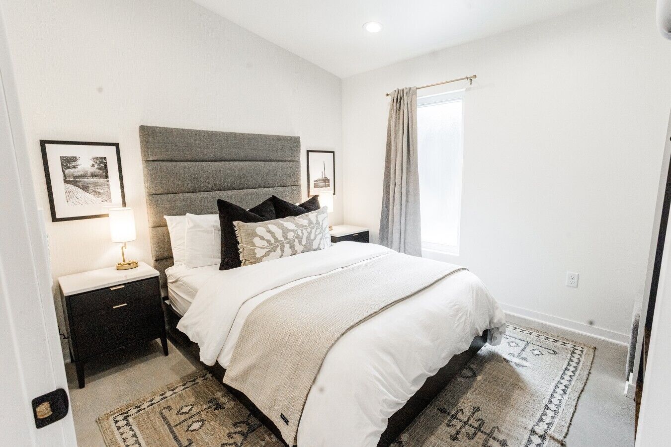Une chambre à coucher avec un lit, des tables de chevet, une lampe, une fenêtre avec des rideaux et un tapis à motifs.