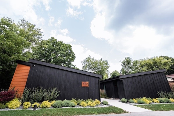 Two modern, black wooden cabins with a number '500' sign, surrounded by well-maintained landscaping and trees.