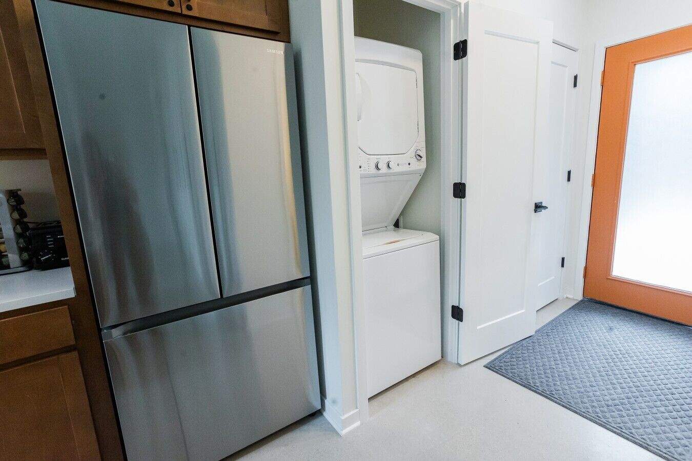 A compact kitchen with a stainless steel refrigerator, a washing machine, and a white door with a black handle.