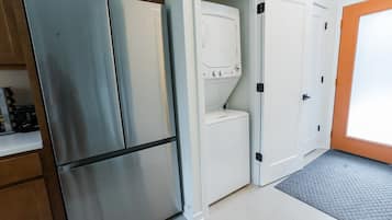 A compact kitchen with a stainless steel refrigerator, a washing machine, and a white door with a black handle.