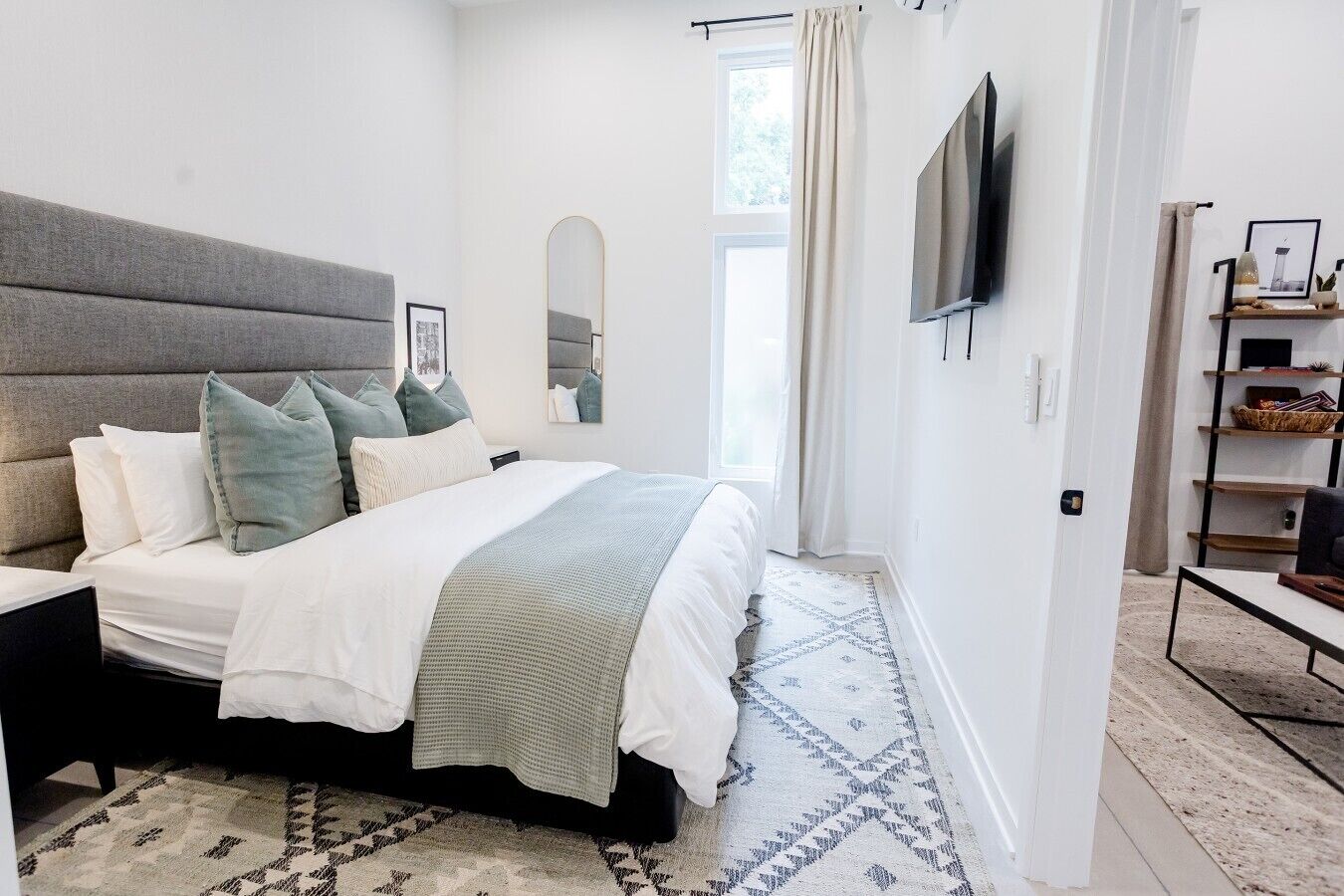 Ein modernes Schlafzimmer mit einem großen Bett, einem Kopfteil, einem Fernseher, einem Spiegel und einem Nachttisch.
