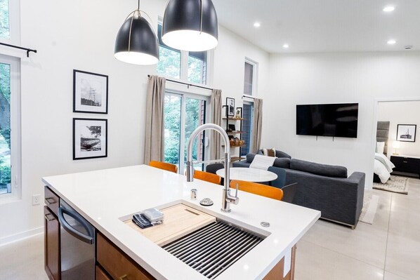 A modern kitchen with a white countertop, a built-in sink, and a window with curtains.