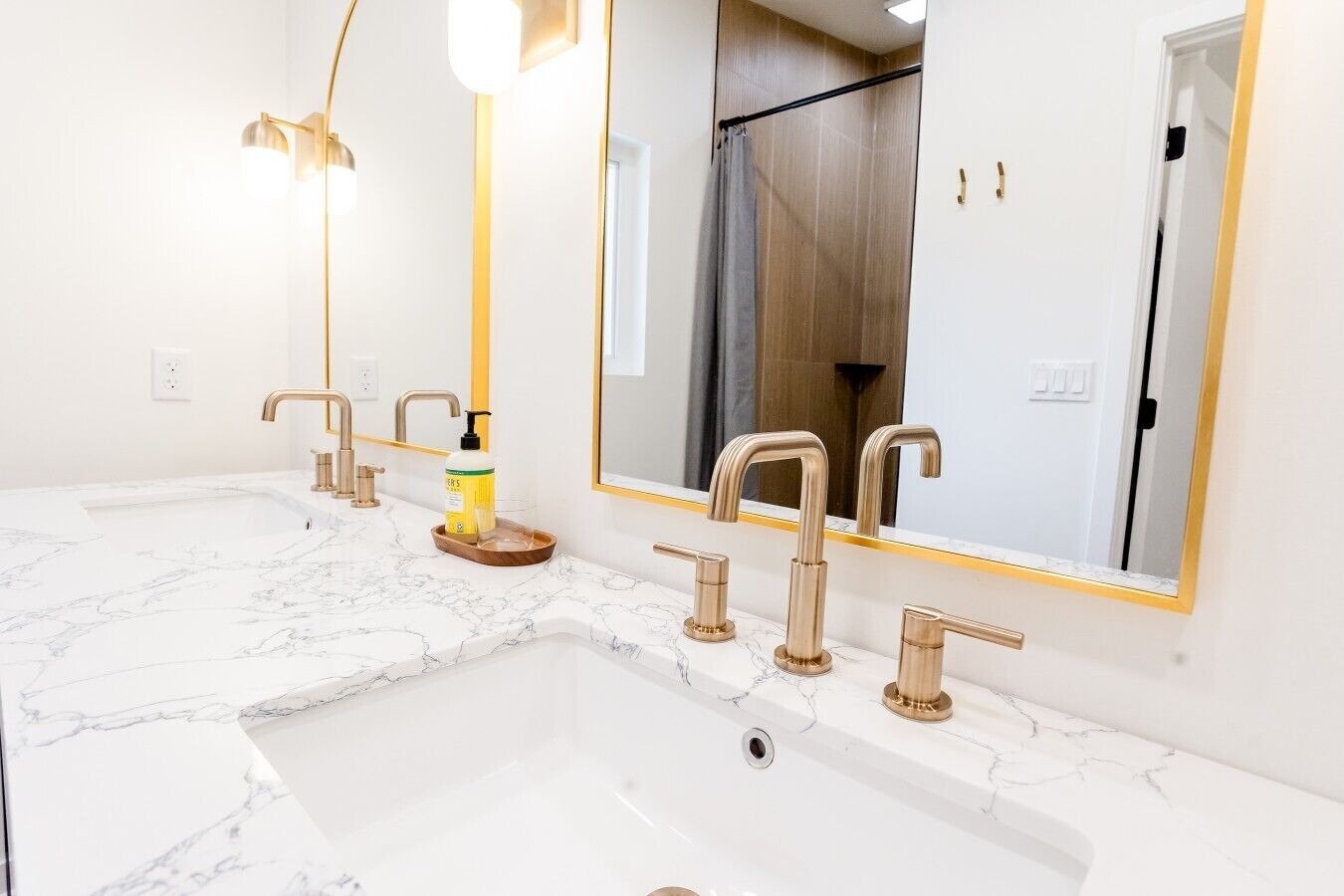 Une salle de bain avec un grand lavabo, plusieurs robinets, un miroir et une douche visible au fond.