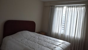 Una camera d'albergo con un letto, un comodino e una finestra con tende.
