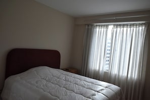 Ein Hotelzimmer mit Bett, Nachttisch und einem fenster mit Vorhängen.