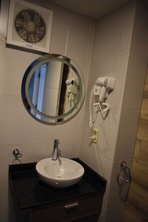 A bathroom with a round mirror, a white sink, a hairdryer, and a wall-mounted fan. - A nice, centrally located apartment in Sopocachi, La Paz. (La Paz)