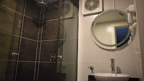 Un bagno con doccia vetro, uno specchio rotondo, un lavandino bianco e un asciugacapelli fissato alla parete.