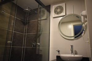 Ein Badezimmer mit einer Duschkabine, einem runden Spiegel, einem weißen Waschbecken und einem an der Wand montierten Fön.