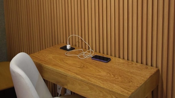 Una parete rivestita in legno, una sedia bianca e un tavolo di legno con uno smartphone e delle cuffie.