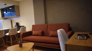 Un ambiente compatto con divano, tavolo da pranzo, un piccolo tavolino e televisore a parete.