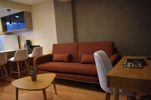 Ein gemütlicher Wohnbereich mit Sofa, Esstisch, kleinem Couchtisch und einem an der Wand befestigten Fernseher.