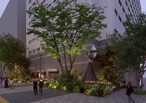 Entrada moderna de hotel con un letrero, una antena parabólica y vegetación circundante.