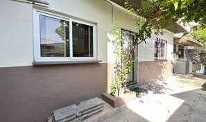 Ein Wohngebäude mit einem Fenster, einer kleinen Grünfläche mit Pflanze und einem Betonweg.