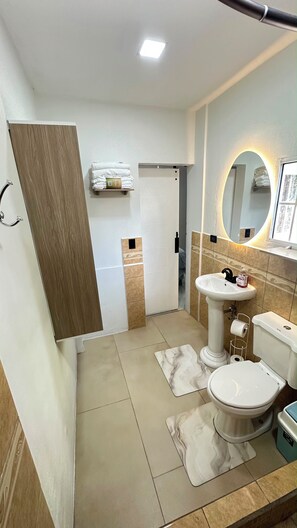 Ein Badezimmer mit Toilette, Waschbecken und Spiegel. Handtuchhalter und Duschbereich vorhanden.