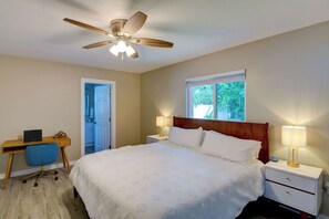 A bedroom with a bed, two bedside tables, a desk with a chair, a ceiling fan, and a window with a view of greenery. - Sarasota Paradise with Private Pool – Minutes to Siesta Key (Sarasota)