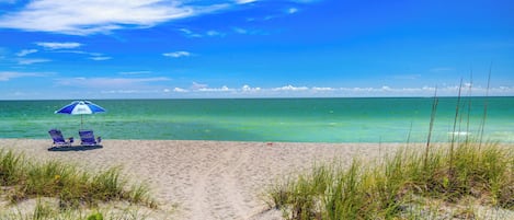 A beach with a clear path leading to the sea, two lounge chairs, and a beach umbrella.