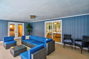 Ein Zimmer mit einem blauen Sofa, Korbstühlen, einem Glastisch und einer Tür zu einem Balkon.
