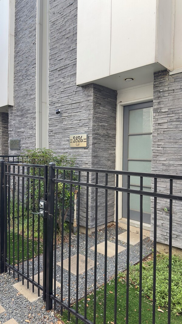 A modern building with a stone facade, a black metal fence, and a small garden area with gravel and grass.