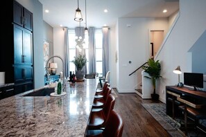 A modern kitchen with a marble countertop, a long dining table, and a staircase leading to an upper level.