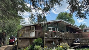 A cabin with a deck, surrounded by trees and a garden. - Château Kozy Kove (Kawartha Lakes)