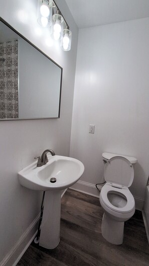 Ein Badezimmer mit einem Standwaschbecken, einer Toilette und einem Spiegel mit Beleuchtung darüber.