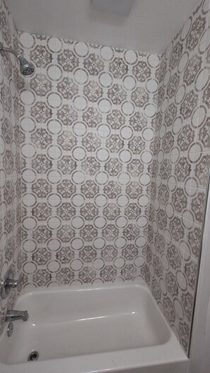 A bathroom with a bathtub, a showerhead, and patterned tiles. - Airport-Adjacent 3 Bedroom 2 Bath Cottage (Charlotte)