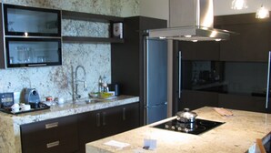 A modern kitchen with dark cabinetry, a granite countertop, a built-in stove, and a stainless steel refrigerator. - Vidanta Golf and Spa Resort 1 bedroom Grand Luxxe suite (Playa del Carmen)
