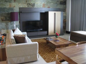 A modern living room with a sofa, coffee table, and a flat-screen TV against a stone wall.