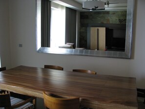 A dining area with a large wooden table and chairs, a large mirror reflecting the room, and a stone fireplace.
